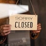 Through glass view of woman business owner hanging up sign with inscription closed at end of working day.