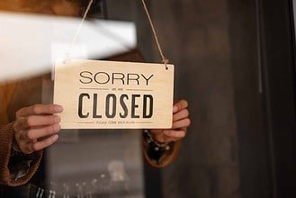 Through glass view of woman business owner hanging up sign with inscription closed at end of working day.