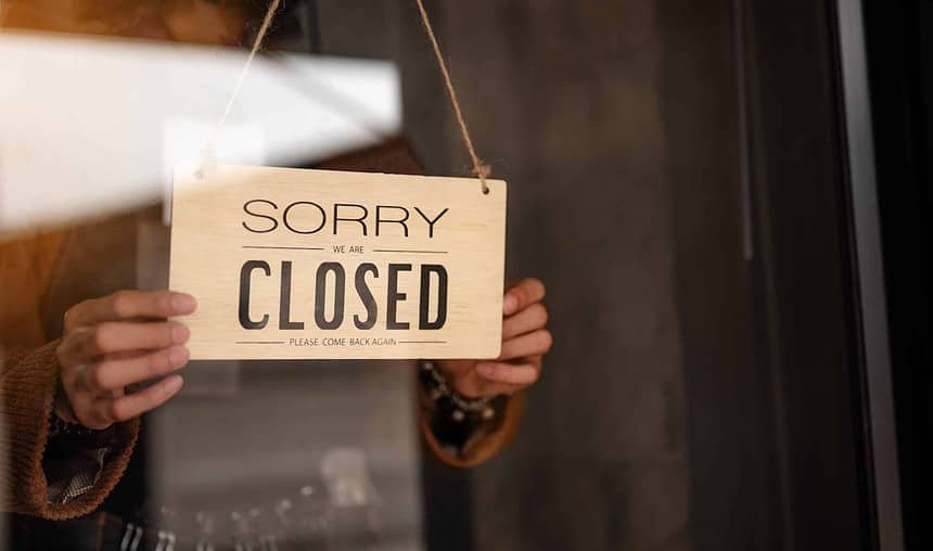 Through glass view of woman business owner hanging up sign with inscription closed at end of working day.